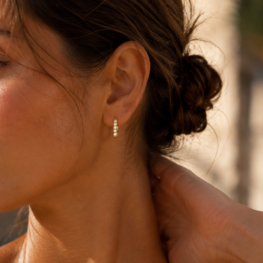 Close-up of a woman with sun-kissed skin, wearing a delicate earring, outdoors.