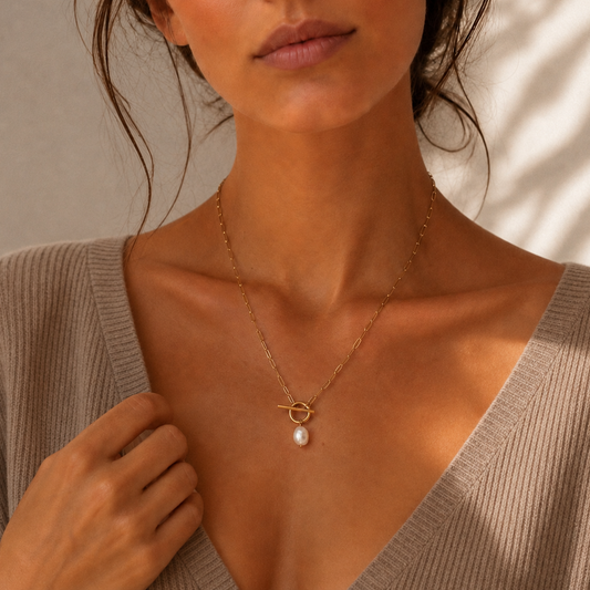 Woman wearing a gold necklace with a pearl pendant against a neutral background